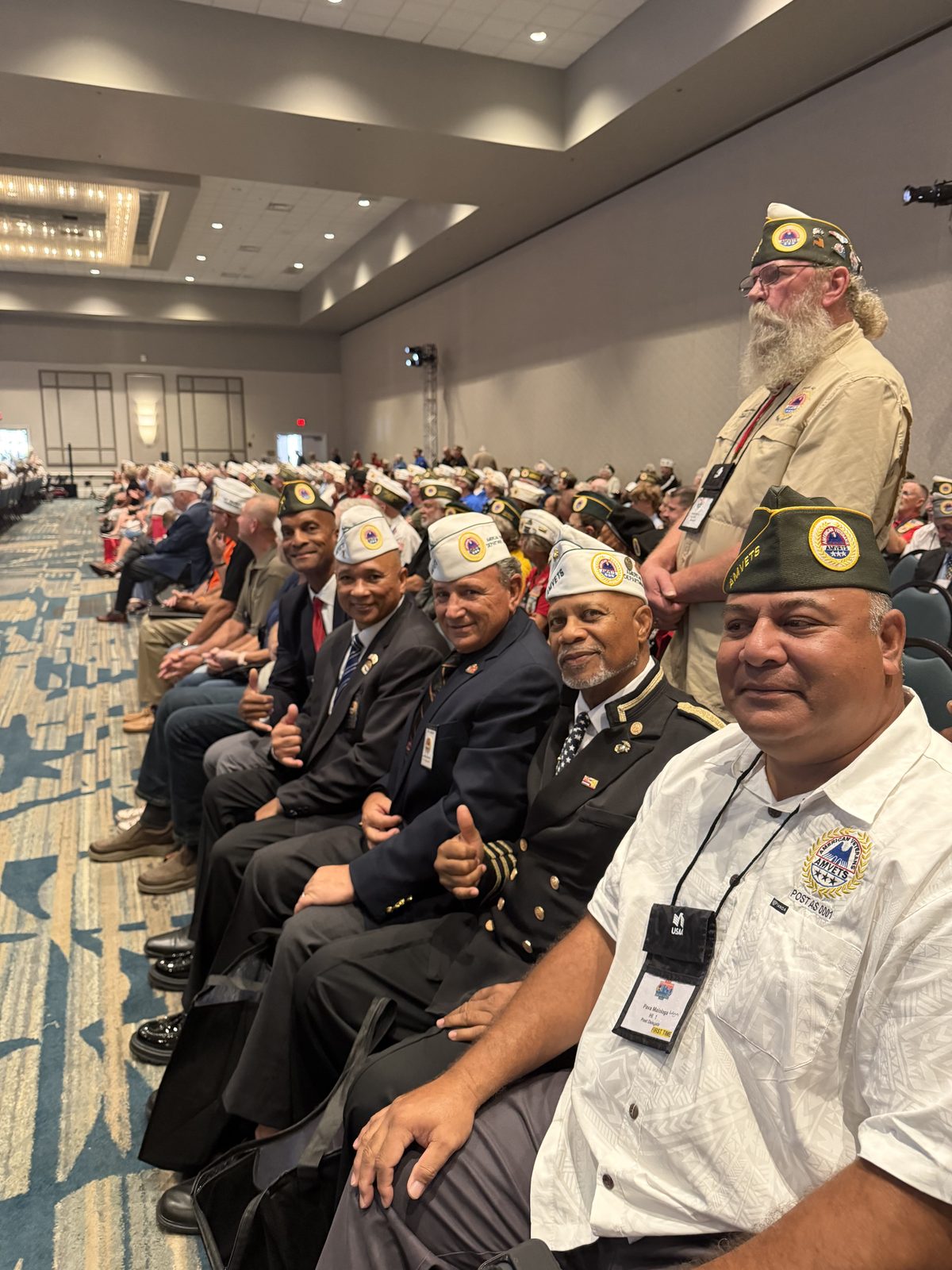 AMVETS members in service caps seated together on the convention floor.